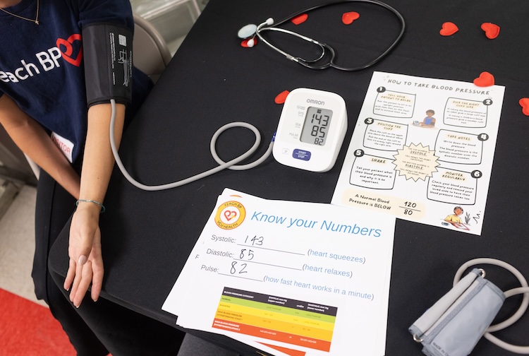 Papers on a table show blood pressure readings, with a person’s arm out with a blood pressure cuff.