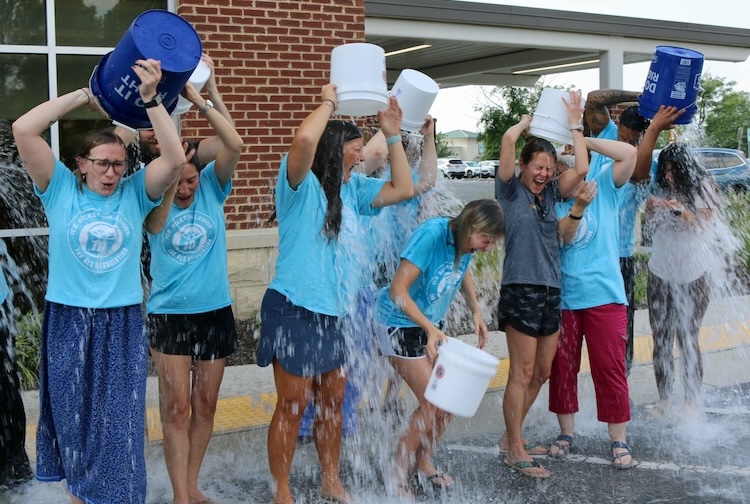 people in blue matching shirts dump buckets filled with ice water on their heads.