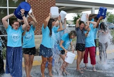 people in blue matching shirts dump buckets filled with ice water on their heads.