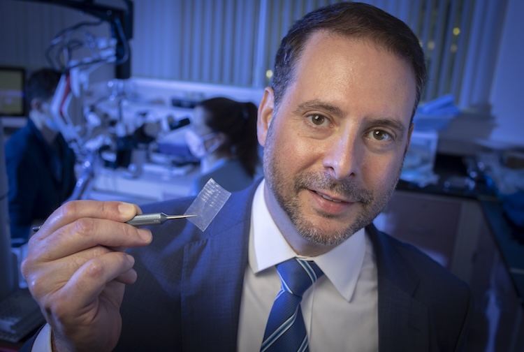 Man holds up tweezers with small piece of tape