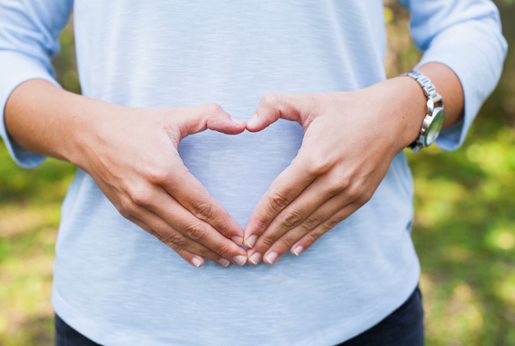 Woman’s hands over belly make a heart shape