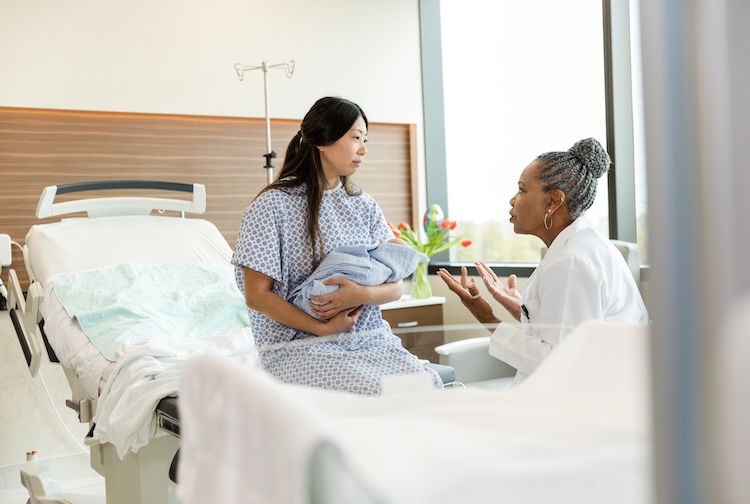 Mother holding a baby speaks to doctor in hospital bed