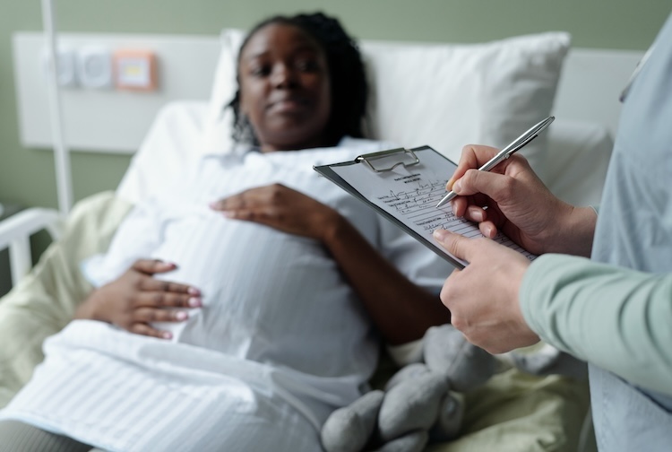 Pregnant woman lying in hospital bed, discussing with doctor holding clipboard and pen.