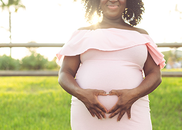 A pregnant lady makes a heart symbol with her hands over her baby bump.