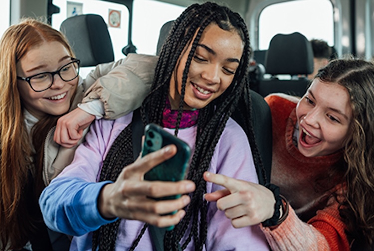 three girls on a bus laughing at a phone