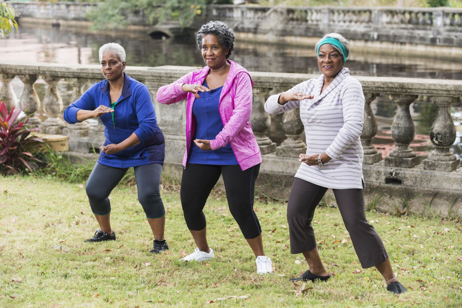 Three women do Tai Chi on grass.