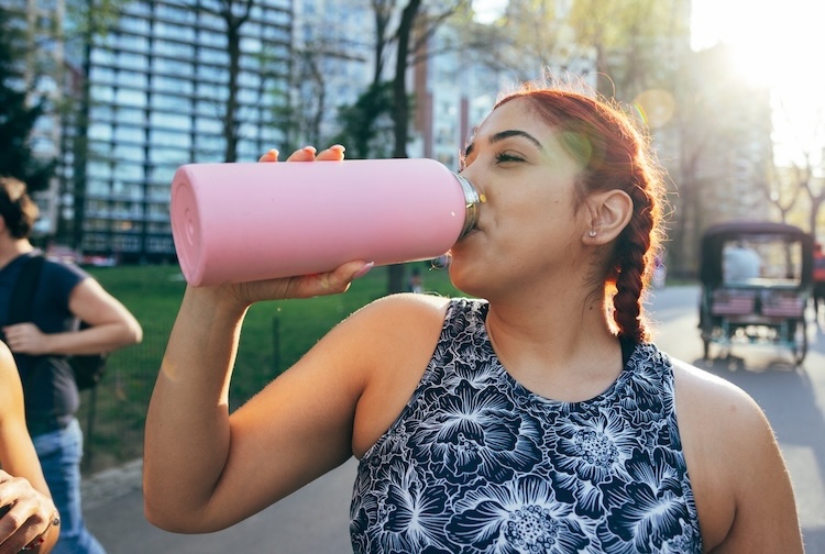 Young woman drinking out of a water bottle on a hot day.