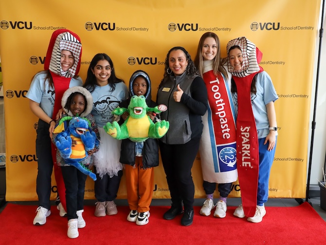 Group of students and children stand for a photo. Students are in costumes that look like tooth brushes.