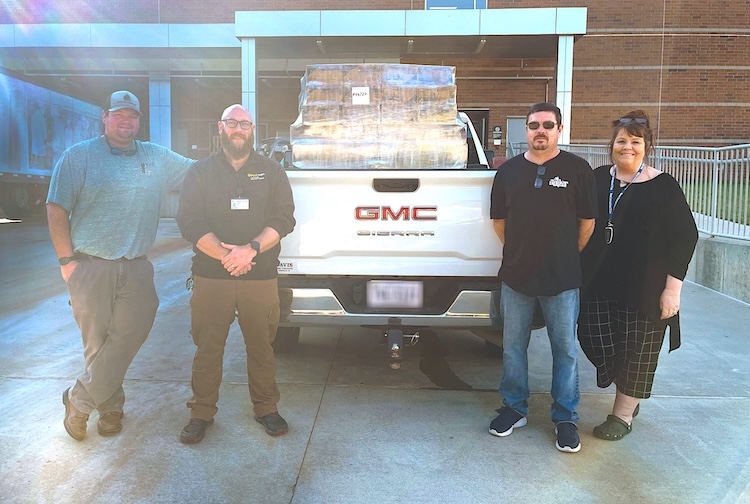 four people stand by a pick up truck filled with boxes of surplus supplies