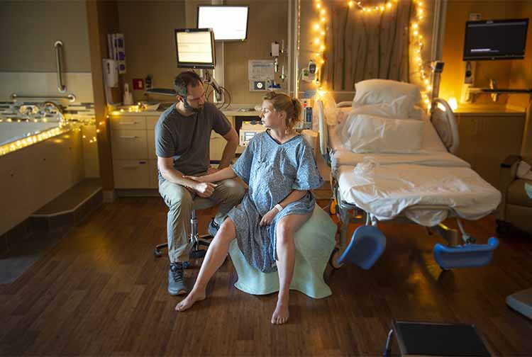 Pregnant woman in hospital gown sitting on exercise ball while doctor speaks to her