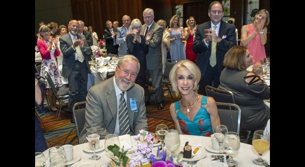 Guest stand and clap to honor Rich and Joyce, who are seated at table.