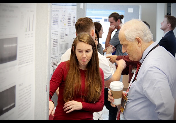 Man talks with student at presentation. 